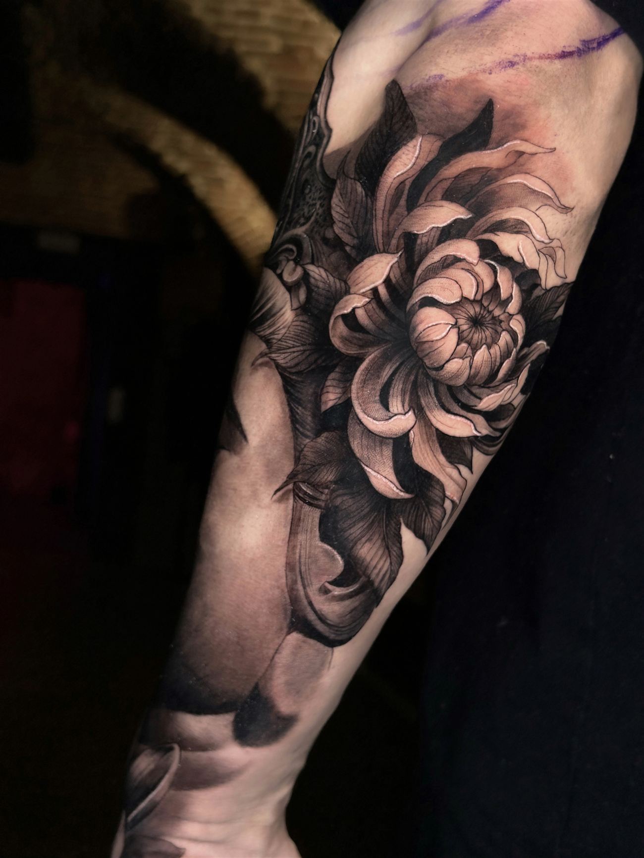 Tatuaje de línea fina de un crisantemo en blanco y negro sobre el antebrazo