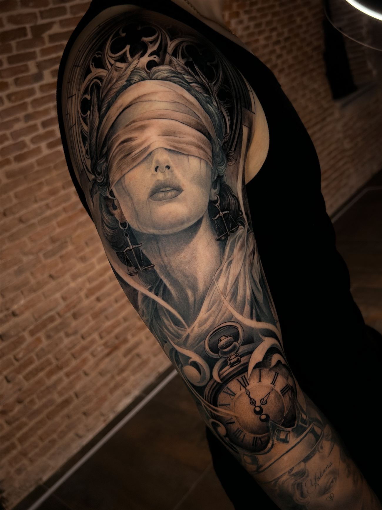 Tatuaje de realismo en blanco y negro de una mujer con los ojos vendados y balanza, junto a un rosetón gótico